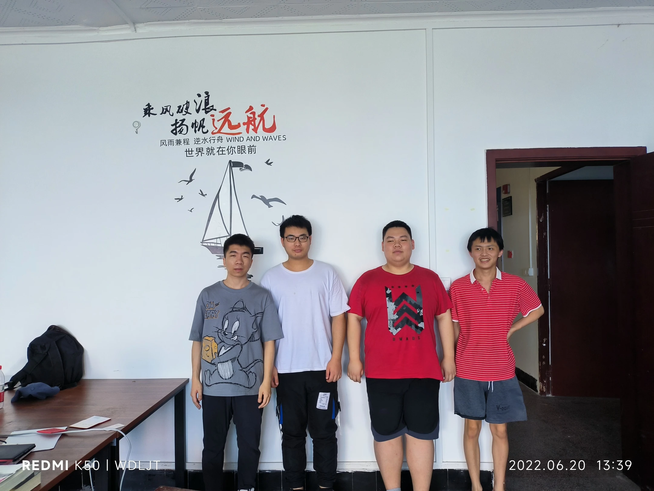 四位队员在写有乘风破浪扬帆远航的墙前合影