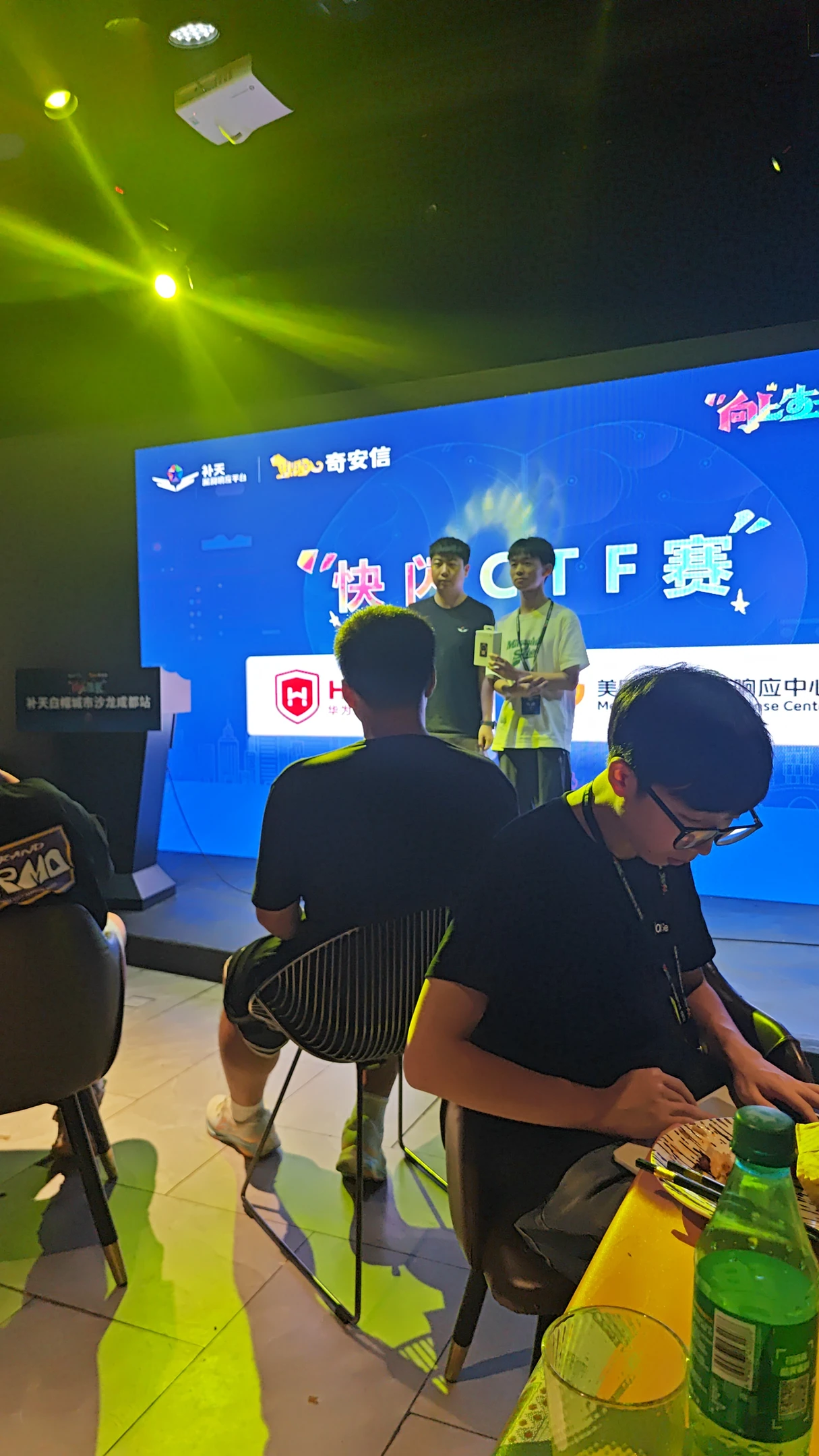 快闪CTF现场，队员在电脑前操作，身后是舞台和参赛者